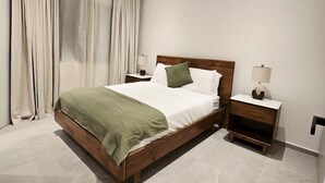 A modern bedroom with a wooden bed, white linens, a green throw, and a nightstand with a lamp. - Soleil & Sage Haven,2BR Townhouse in Cupecoy (Cupercoy)