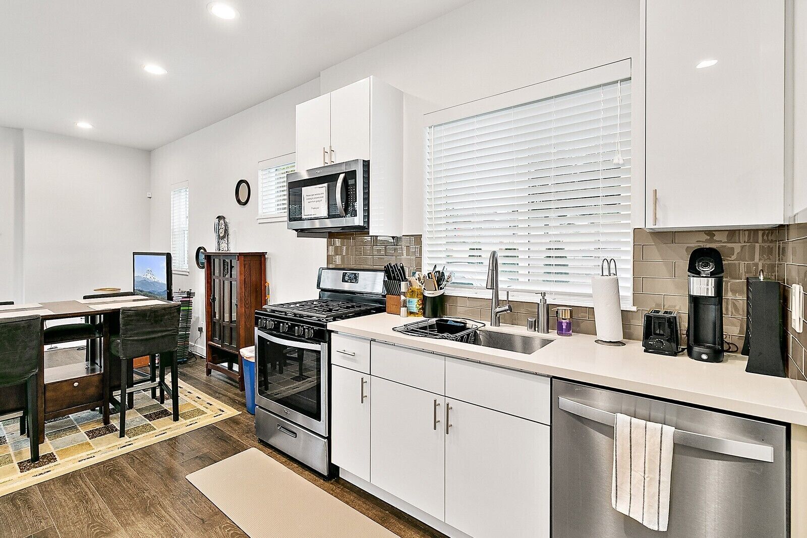 A modern kitchen with white cabinets, stainless steel appliances, and a dining area with a wooden table and chairs.
