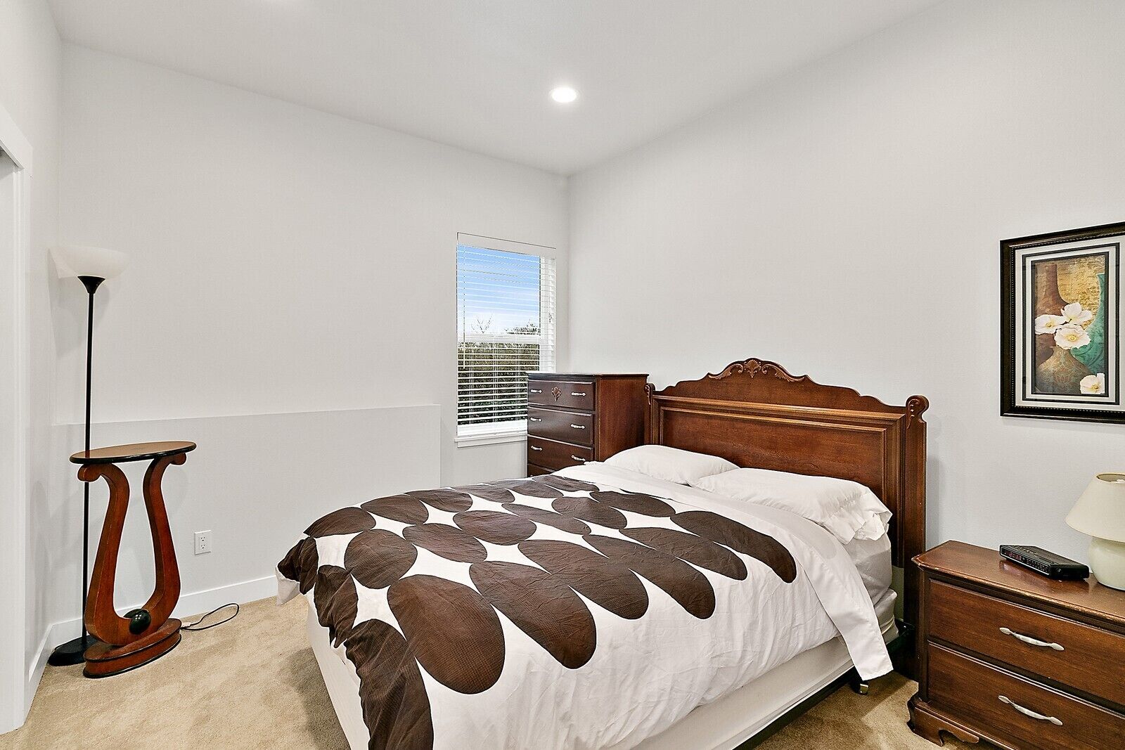 Quarto com cama de madeira, mesa de cabeceira, cômoda, abajur e janela com persianas.