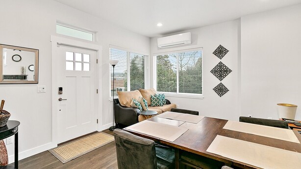 A modern dining area with a wooden table and chairs, a sofa with cushions, and a window with blinds. - 2 Bed MIL unit with Lake Washington views (Seattle)