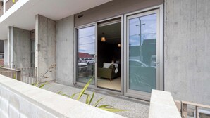 A modern building with large sliding glass doors leading to a room with a bed and a small table. - Petone Studio | Balcony | Near Beach + Shops (Lower Hutt)