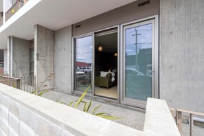 A modern building with large sliding glass doors leading to a room with a bed and a small table. - Petone City Studio with Outdoor Space (Lower Hutt)