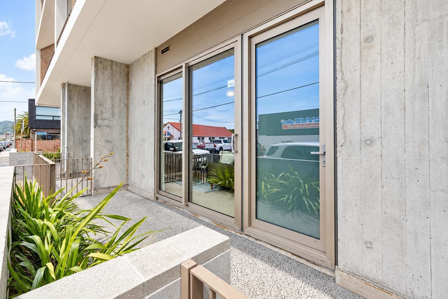 A building with large glass doors, a concrete facade, and a parking lot visible through the windows.