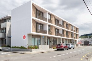 Un immeuble moderne à plusieurs étages, doté de balcons, d’un panneau indiquant un parking et d’un panneau de signalisation indiquant un arrêt.
