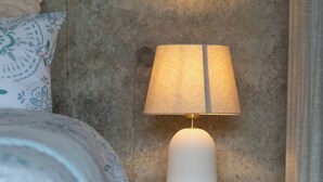 Una cama con ropa de cama estampada, una mesita de noche blanca con una lámpara y una pared con textura.