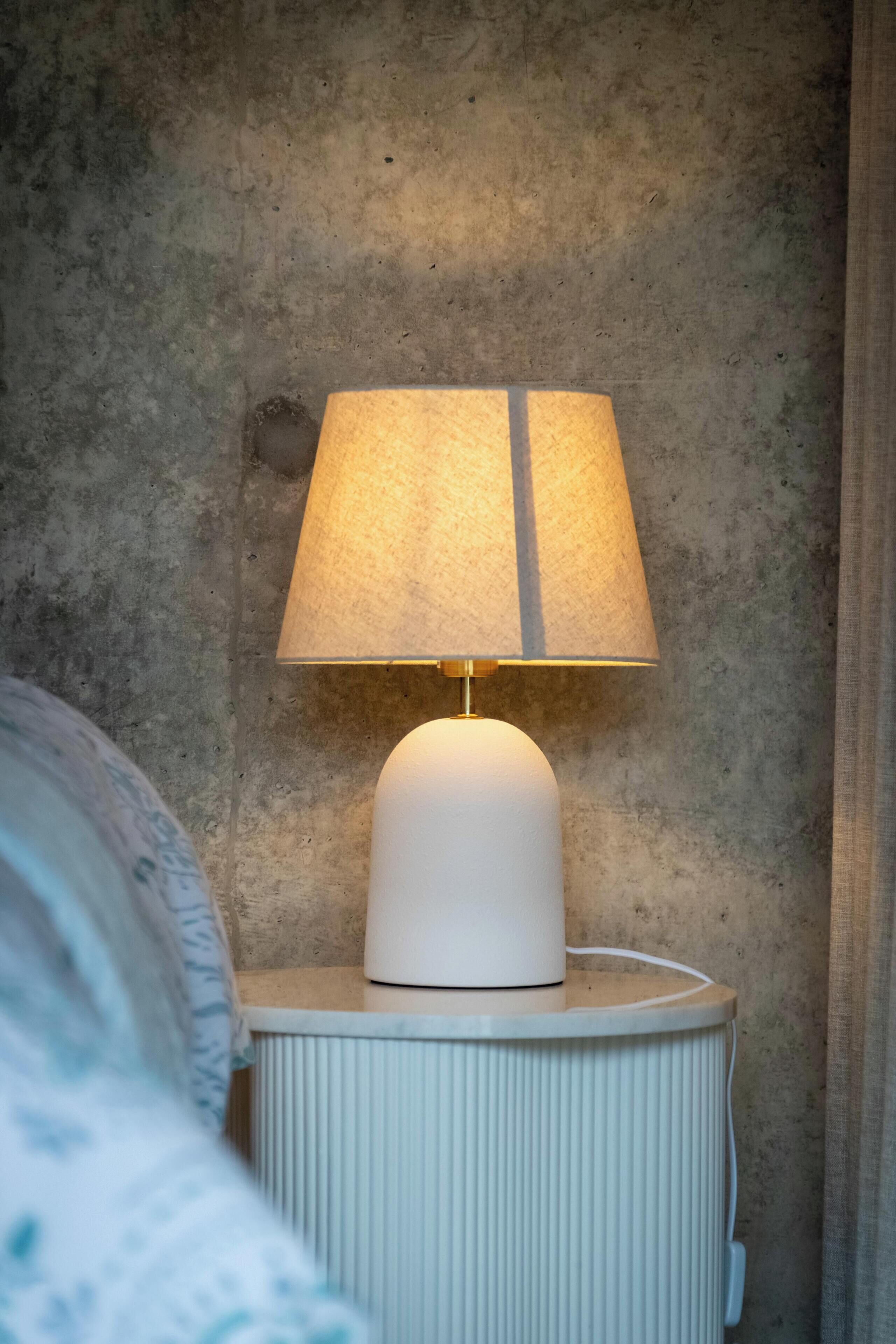 A white bedside table with a lamp and a power outlet.
