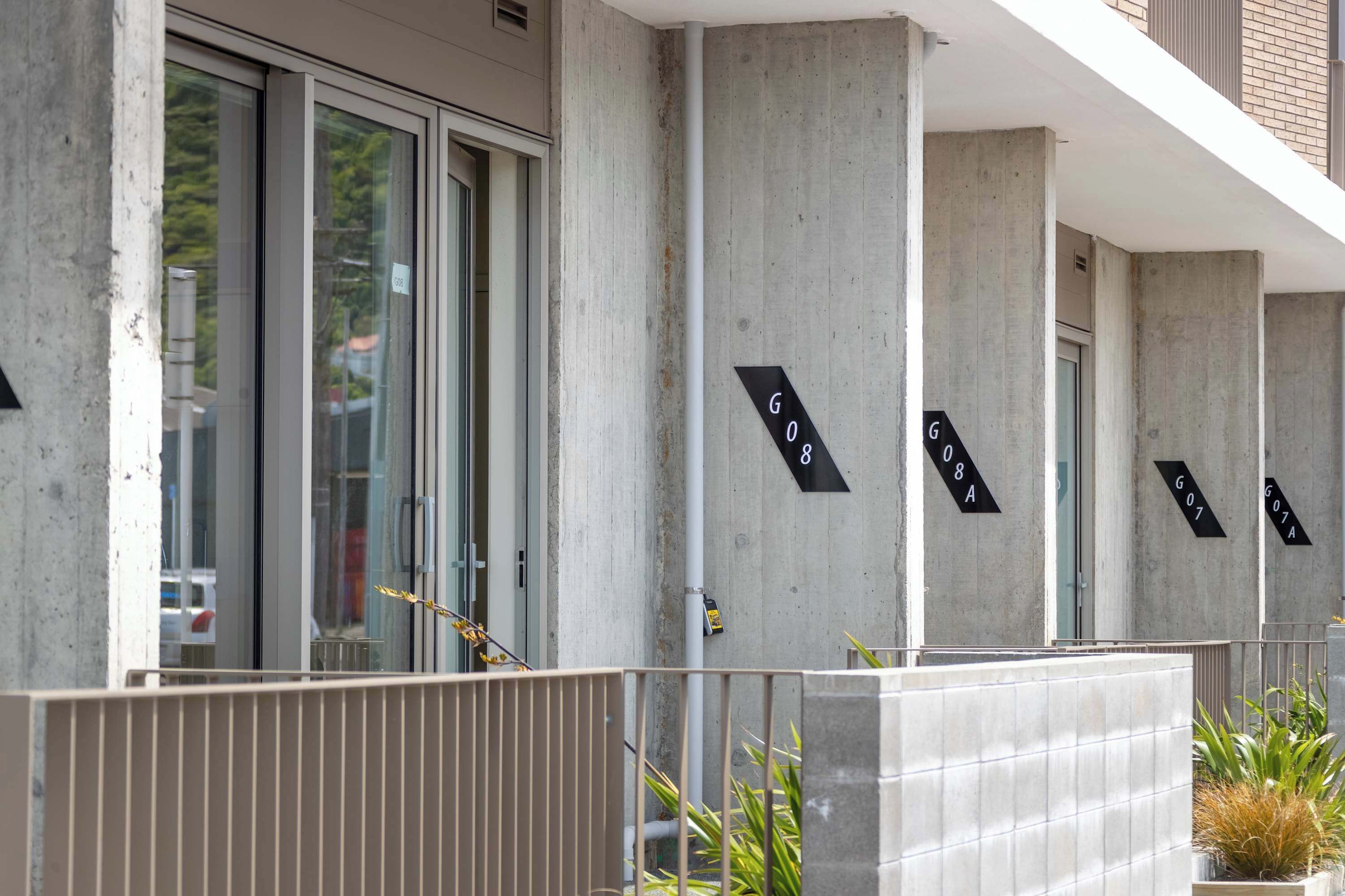 A building facade with concrete columns and large windows, featuring numbered signs indicating unit locations.