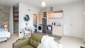 Una habitación de hotel moderna con un sofá verde, una mesa de comedor con sillas, una cocina con refrigerador, lavadora y armarios.
