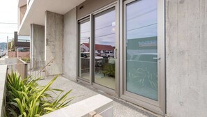A building with large glass windows, a concrete exterior, and a paved entrance area with plants. - Petone Studio | Balcony | Near Beach + Shops (Lower Hutt)