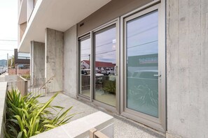 Un bâtiment doté de grandes fenêtres en verre, d’une façade en béton et d’un espace d’entrée pavé agrémenté de plantes.