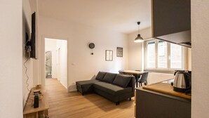 Un soggiorno moderno con un divano modulare grigio, un tavolino in legno e un angolo cottura con un bollitore.