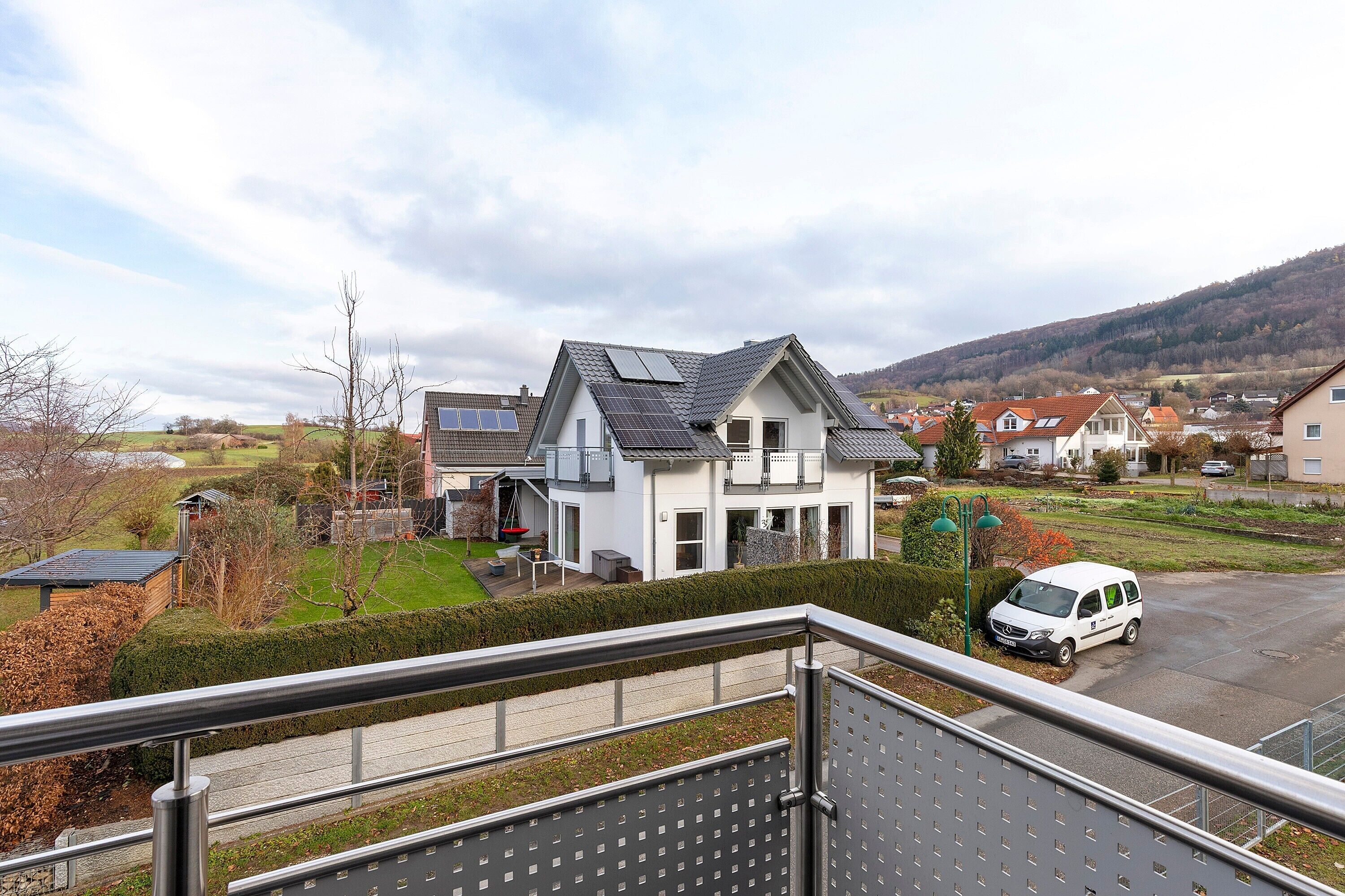 A residential area with a house featuring a sloped roof, solar panels, and a white exterior.