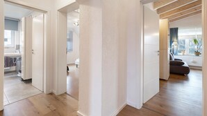 Ein modernes Interieur mit Holzboden, weißen Wänden und einem durch eine offene Tür einsehbaren Küchenbereich.