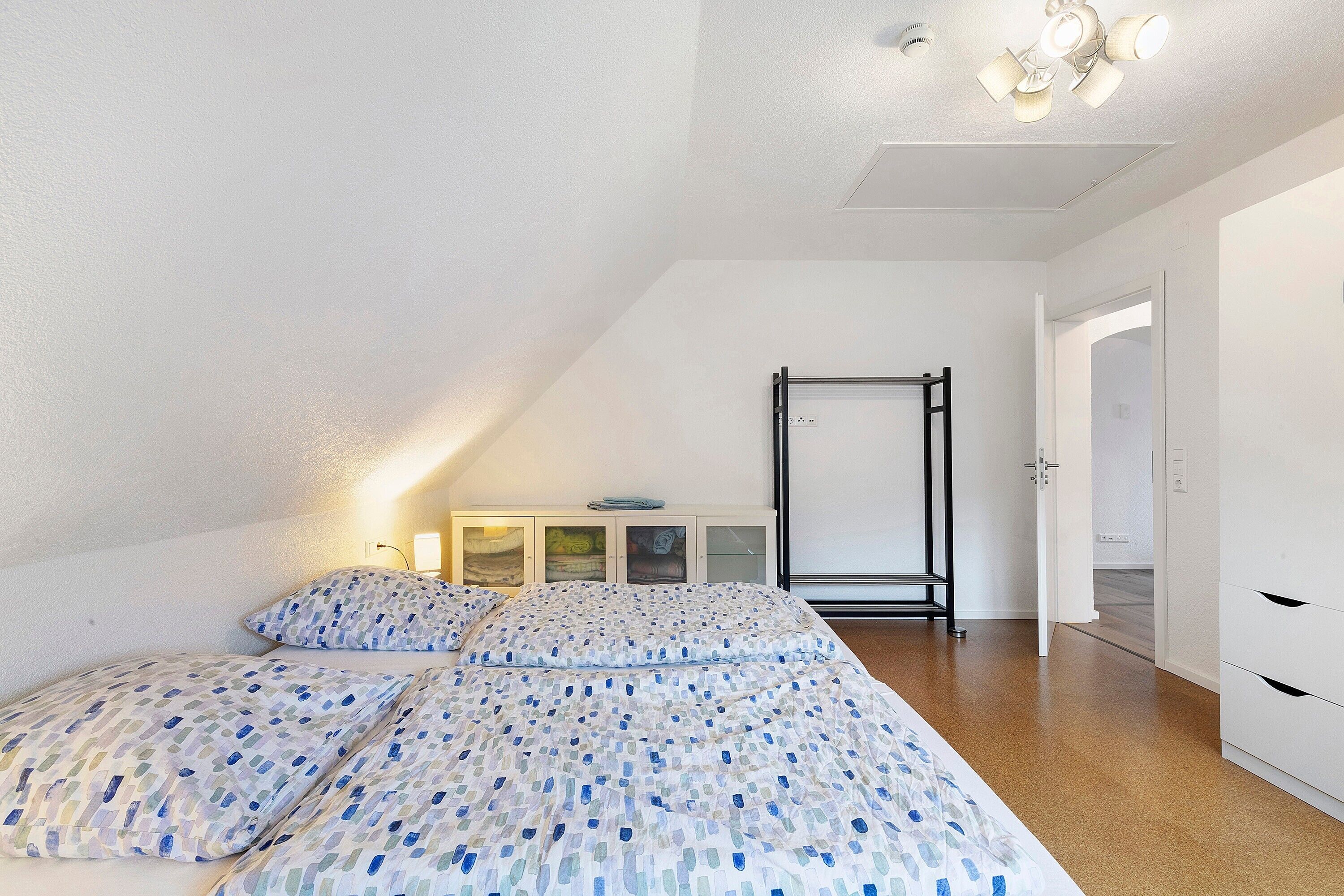 Un dormitorio con una cama, un armario, un escritorio con lámpara y una puerta que da a otra habitación.