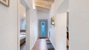 Ein schmales Dielenkorridor mit Holzboden, einem Bett mit weißer und rosa Bettdecke, einer Tür mit Milchglasfenster und einem an der Wand befestigten Spiegel.