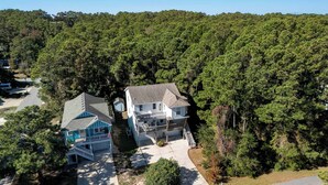 A two-story house with a porch and a garage, surrounded by dense forest. - New Listing, Spacious, King Beds, Linens Provided, Pool Table, KD1310 (Kill Devil Hills)