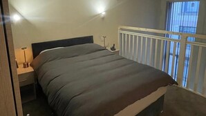Une chambre à coucher avec un lit, une table de chevet, une lampe et une fenêtre avec des stores.