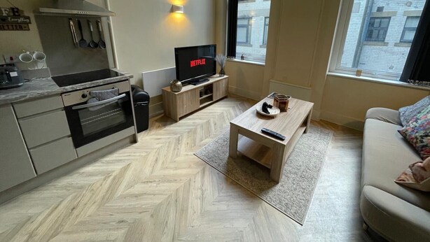 Un espace de vie compact comprenant un coin cuisine, un téléviseur diffusant du contenu « NETFLIX » et une grande fenêtre offrant une vue sur la ville.