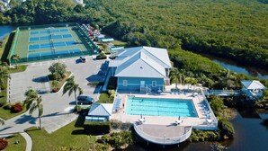 Eine Vogelperspektive zeigt ein Resort mit mehreren Tennisplätzen, einem Schwimmbecken und einem Gebäude mit geneigtem Dach.