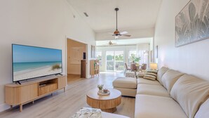 Ein modernes Wohnzimmer mit Flachbildfernseher, einer Holz-Unterhaltungseinheit, einem beigefarbenen Sofa, einem runden Couchtisch und einem Deckenventilator.