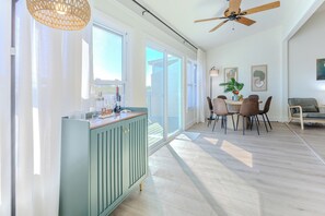 A spacious living area with a dining table, chairs, a ceiling fan, and a large window providing natural light. - Luxury Condo, Heated Pools & Minutes from AMI (Bradenton)