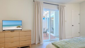 Ein Schlafzimmer mit einem Fernseher auf einer Holzkommode, einem Bett mit grüner Decke und einer Glastür zu einer Terrasse.
