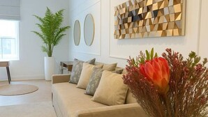 Ett modernt vardagsrum med en beige soffa, ett vitt soffbord och en dekorativ väggdekoration.