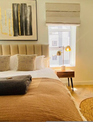 Quarto bem arrumado com uma cama grande, abajur e janela com vista para edifícios.