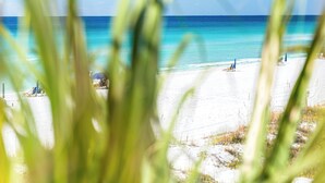 Eine Strandansicht mit klarem, blauem Wasser, weißem Sand und einigen Strandsonnenschirmen.