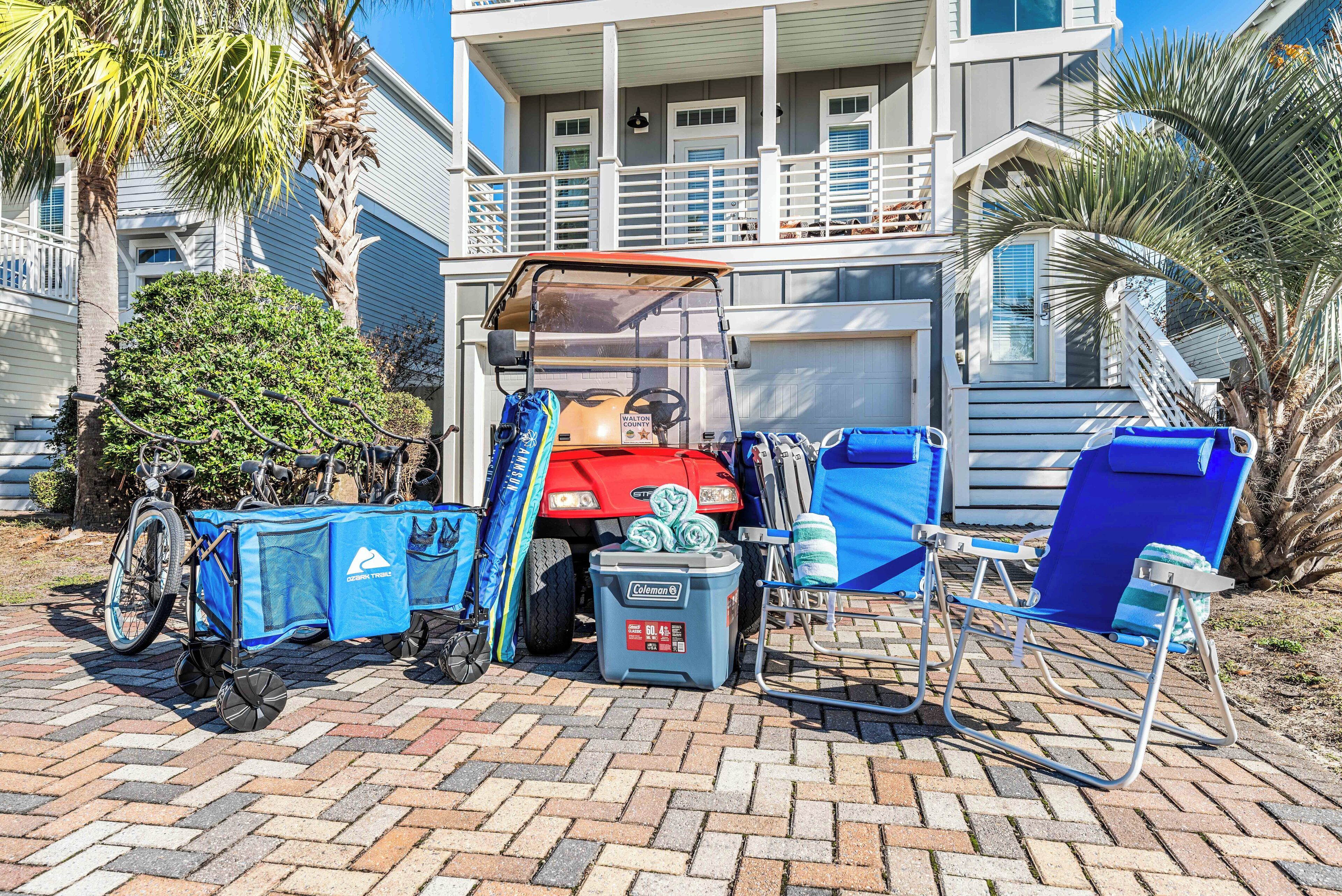 A house with a covered porch, a red vehicle, a bicycle, and outdoor furniture.