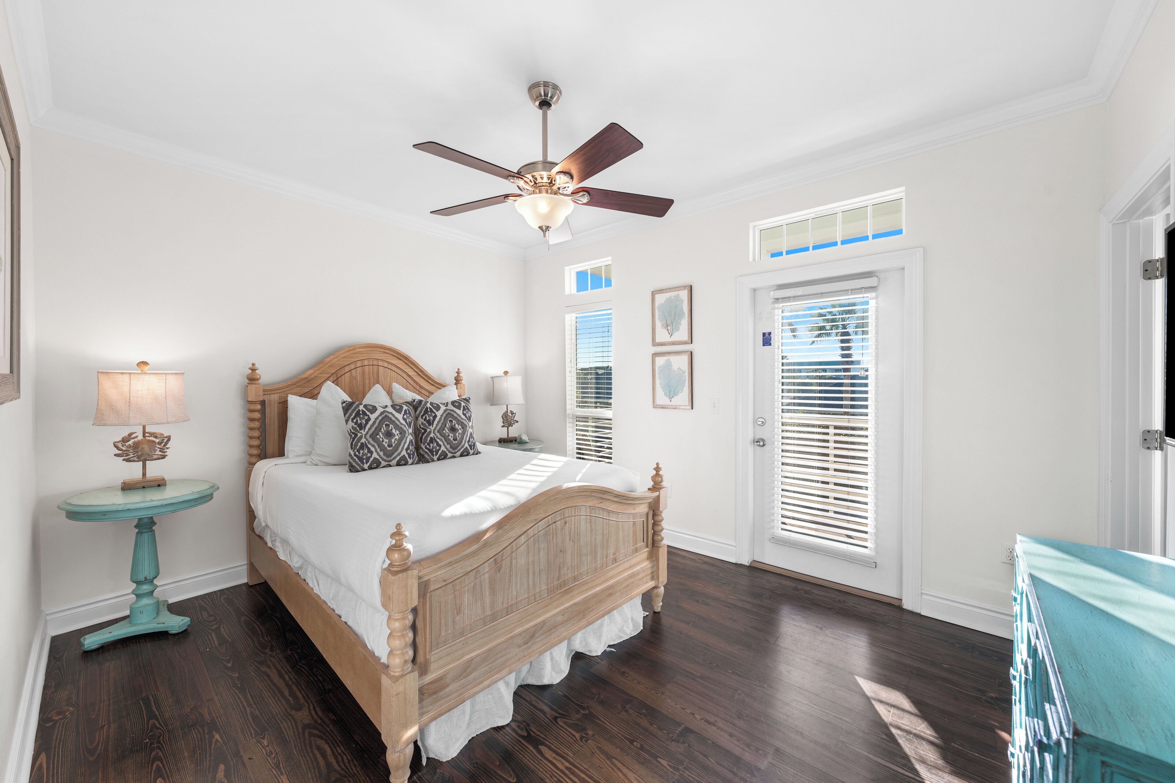 A bedroom with a wooden bed, a ceiling fan, a nightstand with a lamp, and a door with blinds.