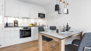 Ett modernt kök med vita skåp, en inbyggd ugn och en matplats med ett bord för fyra personer.