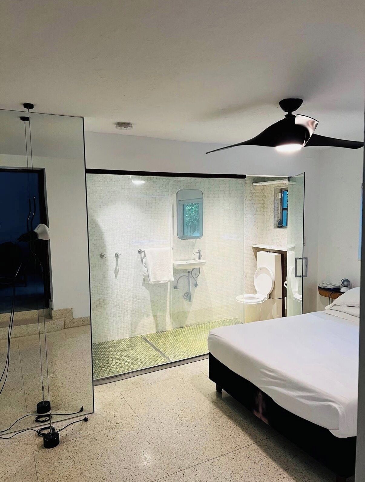 Camera d'albergo moderna con cabina doccia in vetro, servizi igienici separati, lavandino e letto.
