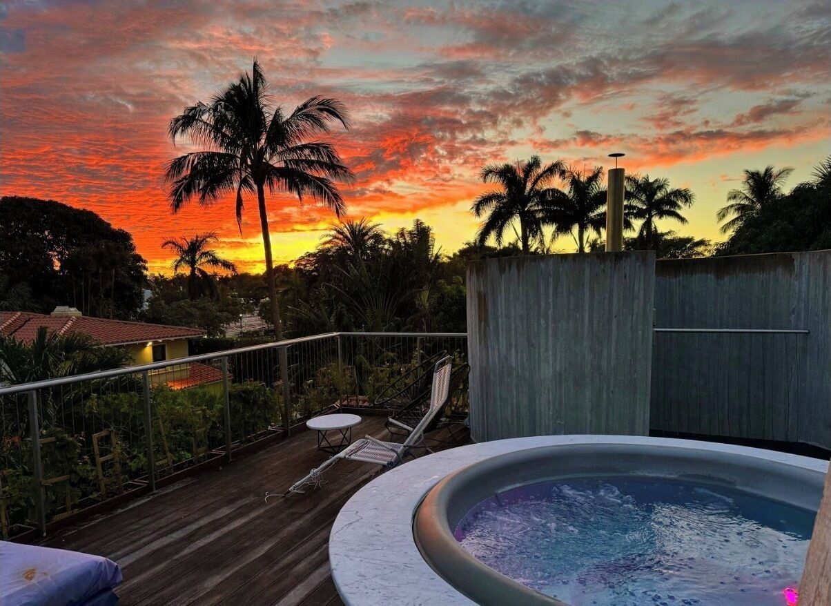Una vasca idromassaggio su un pontile di legno con vista al tramonto, palme e poltrone relax.