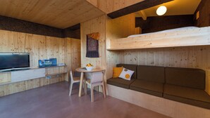Una habitación acogedora tipo cabaña con una cama litera, un televisor, una mesita con un frutero y un sofá con cojines.