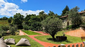 Un jardín ajardinado con un camino de ladrillo, zonas de estar y un edificio de piedra.