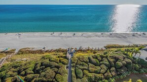 Eine Luftaufnahme eines Strandes mit einem gepflasterten Gehweg, der zu einem Gebäude mit einem langen, schmalen Eingang führt.