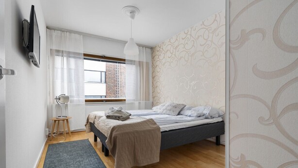 Un dormitorio con cama, escritorio, silla, lámpara y ventana con cortinas.