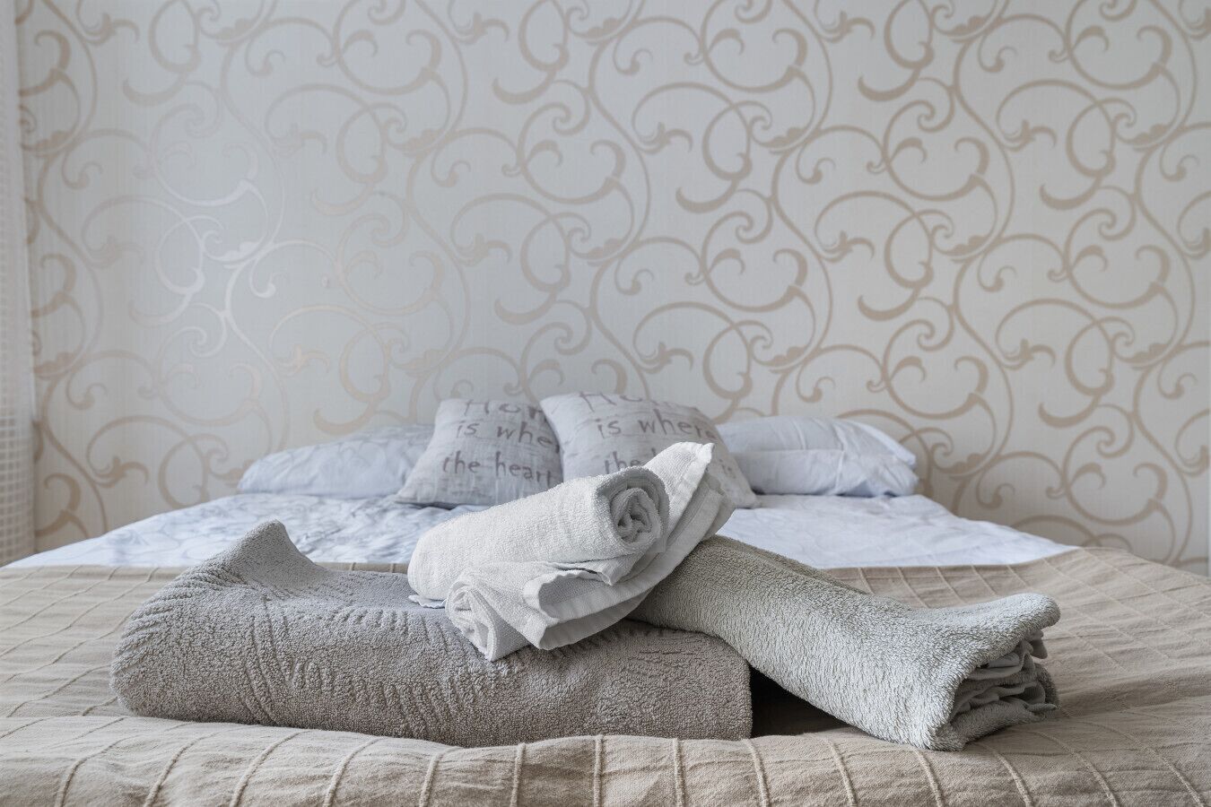 Ein ordentlich bezogenes Bett vor einer Wand mit gemustertem Tapetenhintergrund.