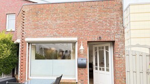 Een bakstenen huis met een groot raam, een deur en een klein terras met een tafel en stoelen.