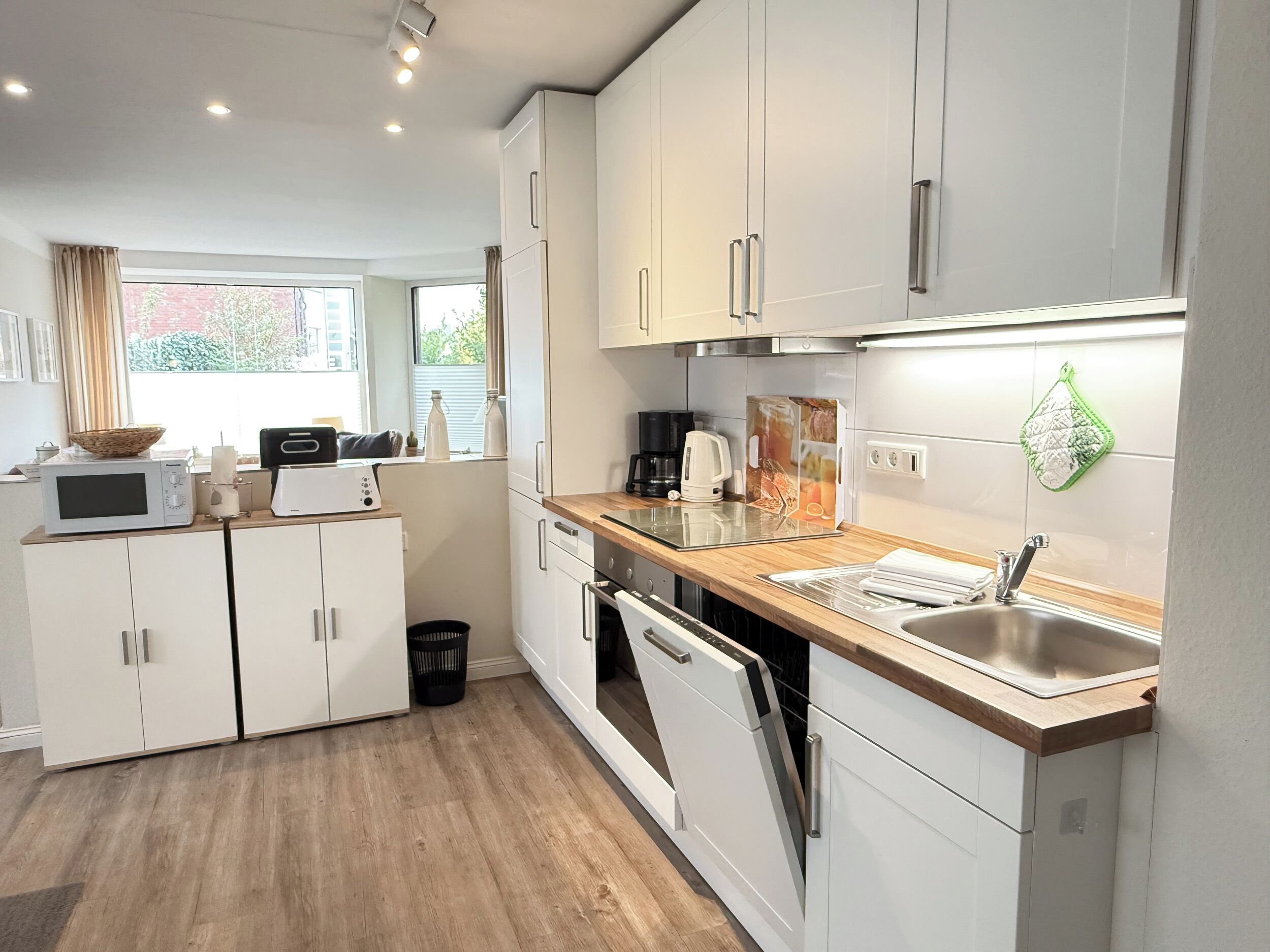 Una cocina moderna con armarios blancos, encimera de madera, horno empotrado y pileta de acero inoxidable.