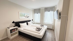 Een moderne slaapkamer met een groot bed, nachtkastjes, een boekenkast en een flatscreen televisie.
