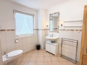 A bathroom with a toilet, sink, and a mirror with a decorative border. - Comfortable vacation apartment in Haus Frida-Sophie with a wood-burning stove, terrace, and garden (Sylt)