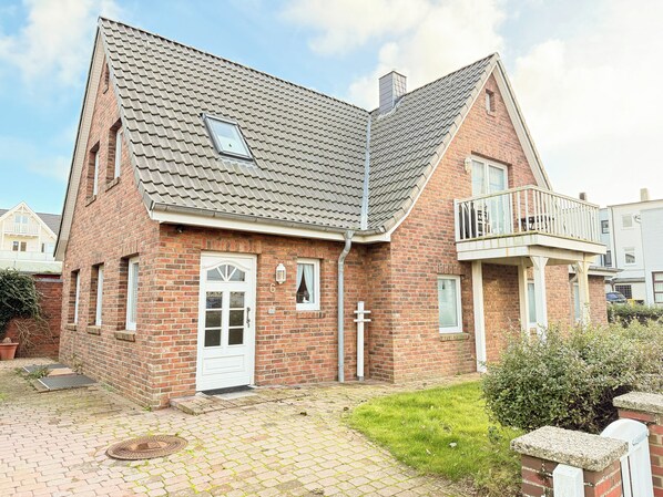 A two-story brick house with a sloped roof, a front door, a small balcony, and a visible number '6' on the wall. - Comfortable vacation apartment in Haus Frida-Sophie with a wood-burning stove, terrace, and garden (Sylt)