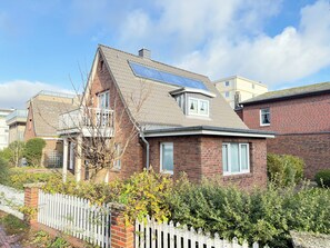 A two-story house with a sloped roof, a visible attic window, and a white picket fence. - Comfortable vacation apartment in Haus Frida-Sophie with a wood-burning stove, terrace, and garden (Sylt)