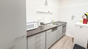 Een moderne keuken met grijze kastjes, een witte achterwand, een magnetron, een koffiezetapparaat en een spoelbak.