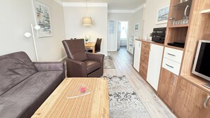 Een moderne woonkamer met een bank, een fauteuil, een salontafel en een keukenhoek met kastjes en een televisie.