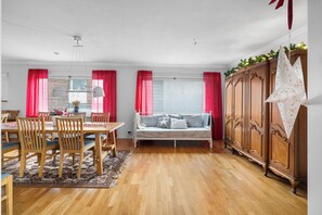 Uma área de jantar com mesa e cadeiras de madeira, um sofá e um armário com uma luminária pendente em formato de estrela.