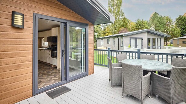 A modern building with a wooden exterior, a glass door entrance, a deck with wicker furniture, and a view of a neighboring house. - Host Stay Beryl Lodge (York)