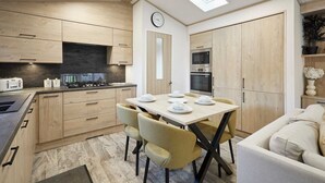 A modern kitchen with wooden cabinets, a dining table with chairs, a clock, and a built-in oven. - Host Stay Hideaway Retreat (York)